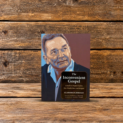 Front cover of The Inconvenient Gospel by Clarence Jordan, featuring an illustrated portrait of Jordan, photographed on a rustic wooden surface.