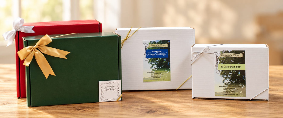 Red, green and two white Koinonia Farm gift boxes tied with ribbon on a wooden table