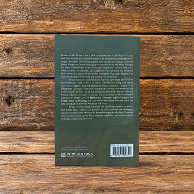 Back cover of Sermon on the Mount by Clarence Jordan, showing the book description and author biography against a rustic wooden background.