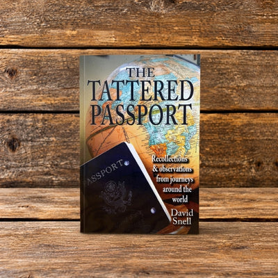 The Tattered Passport by David Snell, showing a globe and passport on the book cover, photographed on a rustic wooden surface.