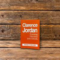 Front cover of Clarence Jordan: Turning Dreams into Deeds by Henlee H. Barnette, featuring an orange book cover, photographed on a rustic wooden surface.